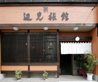 Traditional wooden lattice entrance with white noren and potted plants at Henmi Ryokan in Hokkaidō
