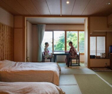Tatami room with twin beds and guests in yukata at Hibikino overlooking garden in Gunma