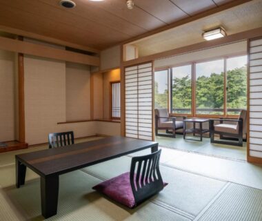 Traditional tatami room with low table, zabuton seating and shoji screens overlooking tree-lined greenery