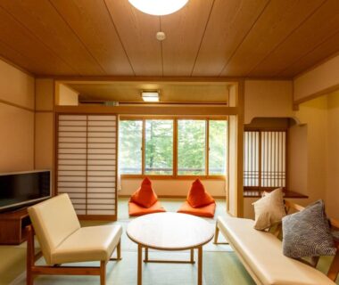 Tatami room with low table, shoji screens, lounge chairs and greenery outside at Hibikino, Gunma