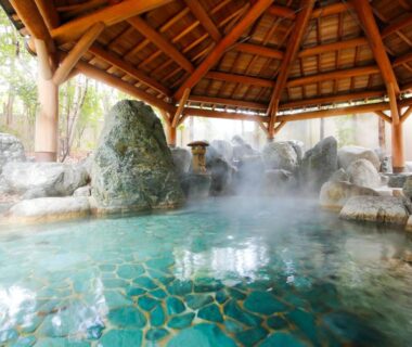 Steaming tiled onsen pool with rock features under wooden roof at Hida Takayama Green Hotel, Gifu