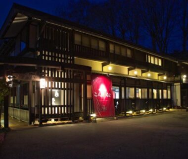 Illuminated wooden ryokan facade with red noren at entrance in Hidatakayama, Gifu