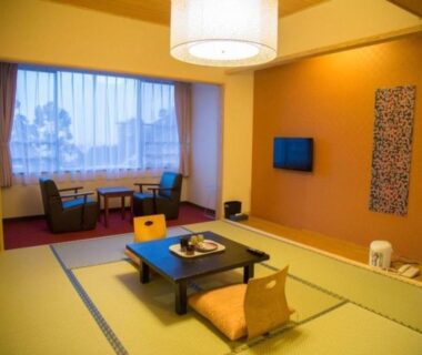 Spacious tatami room with low table, cushions, chairs by window and wall-mounted TV at Higashiyama Park Hotel Shinfugetsu