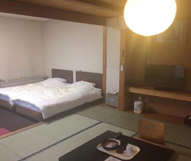 Traditional tatami room with two low beds, low table with tea set, TV cabinet and soft overhead lighting