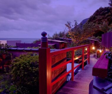 Evening wooden walkway with lanterns leading to outdoor baths and coastal view at Hiina, Shizuoka