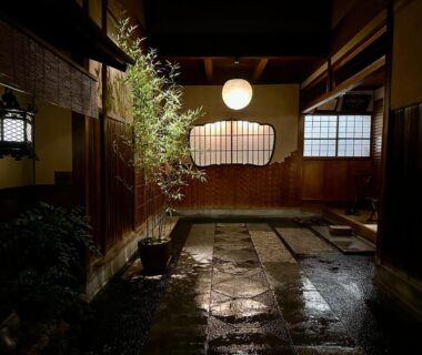 Stone pathway with potted plant and wooden walls illuminated by lanterns at Hiiragiya Kyoto