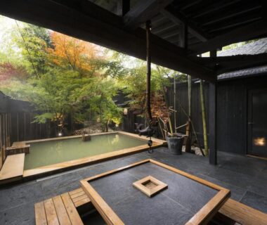 Outdoor onsen bath in courtyard with wooden deck, low seating table and maple foliage