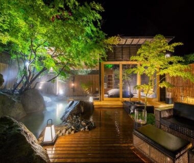 Nighttime outdoor onsen with wooden deck, lanterns and seating at Hikyou Shirakawagensen Sansou Takefue in Kumamoto