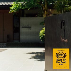 Black entrance sign with award sticker beside pathway and greenery leading to Hinatamikan ryokan entrance in Gunma, Kantō