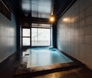 Indoor tiled onsen bath with wooden lattice window and soft lighting at Hinatamikan, Gunma, Kantō
