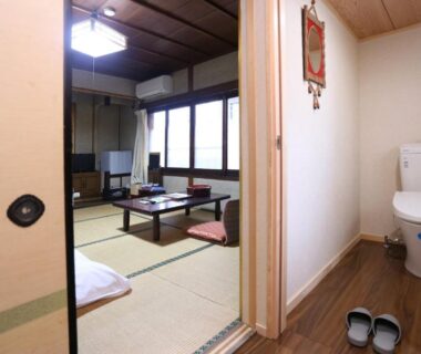 Traditional tatami room with low table and adjacent toilet at Hinode Ryokan in Mie
