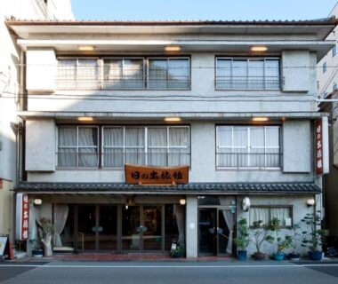 Three-story ryokan facade with traditional entrance and wooden signboard on a downtown Mie street