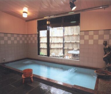 Tiled indoor onsen bath with wooden bucket and bamboo-screened window at Hinodeya in Shizuoka