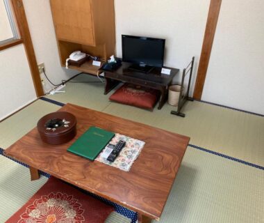 Tatami room with low wooden table, zabuton cushion, TV stand, tea set and tatami flooring at Hinodeya, Shizuoka