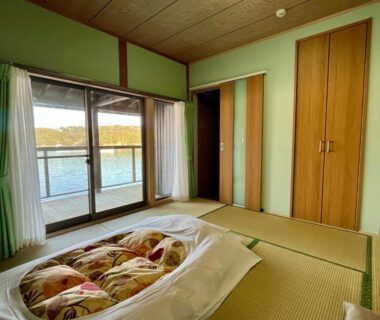 Tatami room with futon and sliding glass doors to balcony overlooking water at Hiogiso in Mie