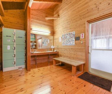 Wood-paneled onsen changing area with lockers, bench and washbasins at Hirayama Onsen Ryokan Kadoya in Kumamoto