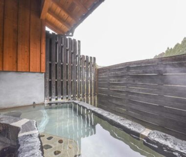Wood and stone outdoor onsen with privacy fence at Hirayama Onsen Ryokan Kadoya in Kumamoto, Kyūshū