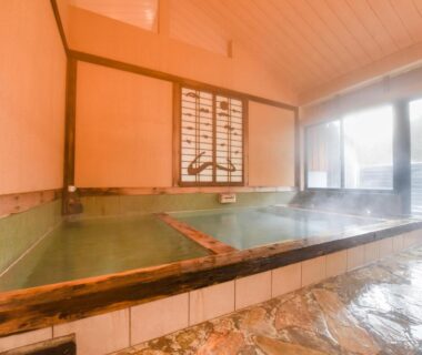 Steaming indoor onsen bath with wooden trim and shoji window at Hirayama Onsen Ryokan Kadoya, Kumamoto