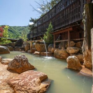Outdoor stone onsen with wooden baths and mountain backdrop at Hirayukan, Gifu, Chūbu, Japan