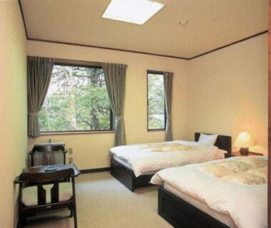 Twin beds and seating area with windows overlooking trees at Hirayunomori Gifu Chubu