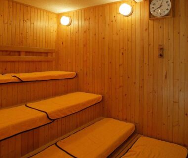 Tiered wooden sauna with cushioned benches and wall clock at Hirayunomori in Gifu, Chūbu