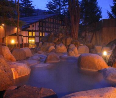 Evening rock-lined outdoor onsen at Hirayunomori with lantern lighting and wooden building in Gifu, Chūbu, Japan