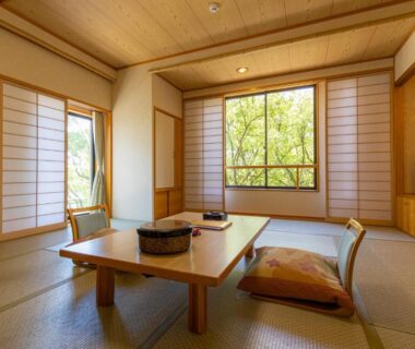 Traditional tatami room with low table, zabuton cushions, shoji screens and garden-view window at Hiroshima no Yado Aioi