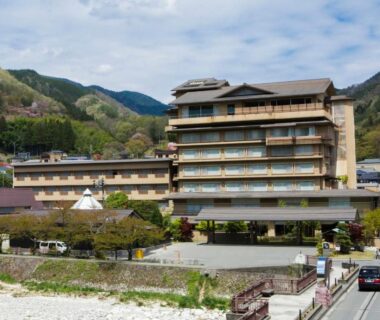 Multi-story ryokan with balconies beside a river and mountain backdrop in Nagano, Chūbu