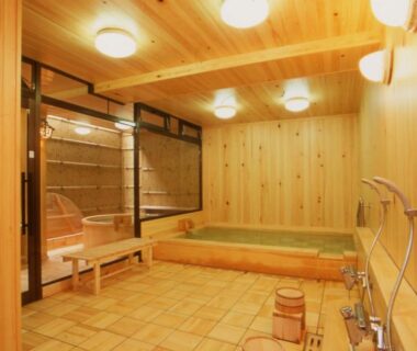 Indoor wooden onsen bath with soaking tub, shower area and stools at Hitomaru Kadan in Hyōgo, Kansai
