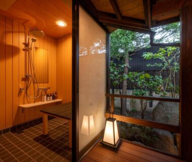Interior wooden bathing area with shower and sliding door opening to small garden courtyard with lantern and greenery