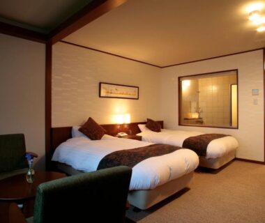 Twin beds with seating area and interior bath viewing window at Suimeikaku ryokan, Hokkaidō