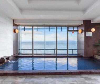 Indoor onsen pool with large windows overlooking the sea at Hokkawa Onsen Hotel in Shizuoka