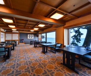 Dining room with tables, large windows overlooking the coast at Hokkawa Onsen Hotel in Shizuoka