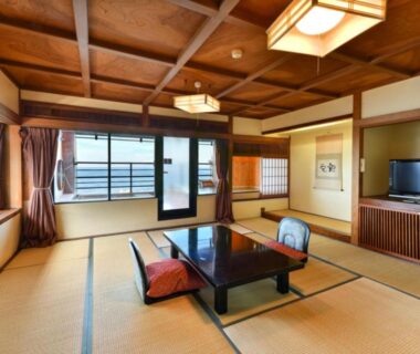 Tatami room with low table, floor cushions, sliding glass doors and wooden ceiling at Hokkawa Onsen Hotel Shizuoka