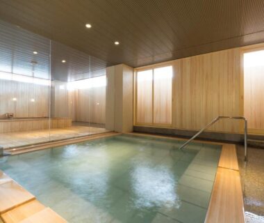 Indoor onsen bath with wooden panels, steps and handrail at Hokuriku Yamashiro Onsen Hotel Kikyou in Ishikawa