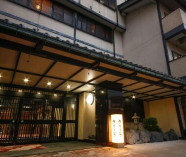 Traditional ryokan entrance with wooden lattice doors, stone lantern and illuminated sign at Hokuriku Yamashiro Onsen Hotel Kikyou in Ishikawa