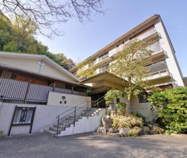 Multi-story ryokan building Honjin with entrance steps, stone landscaping and hillside greenery in Shizuoka