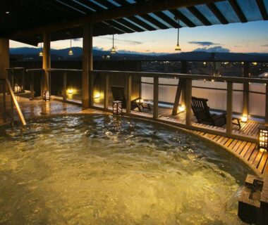 Outdoor onsen bath with wooden deck and lanterns at Honjin Hiranoya Kachoan, Gifu overlooking city and mountains