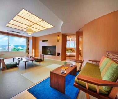 Tatami room with low table, cushioned chairs and large windows overlooking green landscape at Honjin Hiranoya Kachoan Gifu