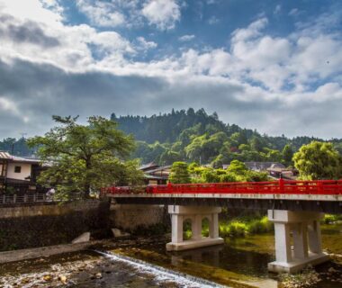 Red arched bridge spanning river with traditional buildings and mountain backdrop near Honjin Hiranoya Kofukan Gifu Prefecture
