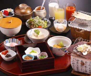 Assorted Japanese breakfast set on lacquer tray with small tabletop grill, rice bowls, side dishes and fruit juices at ryokan