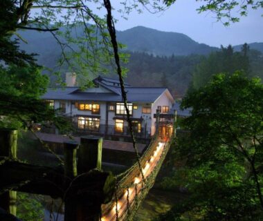 Illuminated wooden footbridge leading to Honke Bankyu with mountain backdrop in Tochigi