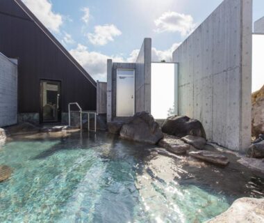Outdoor onsen bath with stone edging and concrete walls under blue sky at Horohoro Sanso, Hokkaidō