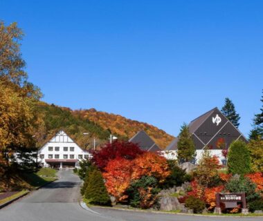 Ryokan exterior framed by autumn foliage, driveway and forested mountain backdrop at Horohoro Sanso in Hokkaidō