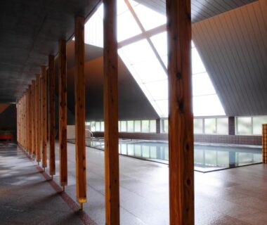 Spacious indoor onsen pool with wooden columns, vaulted skylight ceiling and polished stone floor at Horohoro Sanso, Hokkaidō
