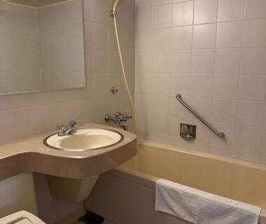 Tiled compact bathroom with bathtub, handheld shower, sink, mirror, grab bar and towel at Horoshin Onsen Hotarukan, Hokkaidō