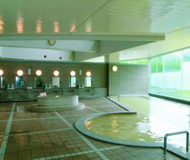 Spacious tiled indoor onsen with round soaking tub, wash stations and large windows at Horoshin Onsen Hotarukan Hokkaidō