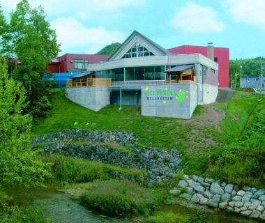 Modern ryokan exterior on grassy slope beside a stream, Horoshin Onsen Hotarukan, Hokkaidō Japan