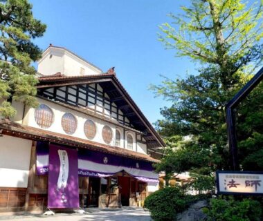 Entrance of Hoshi ryokan with purple noren, wooden facade and trees in Ishikawa, Chūbu region