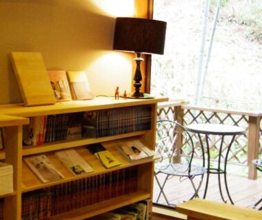 Interior reading corner with bookshelf, lamp and low bench opening to balcony with small table at Hoshi Meguri, Shizuoka